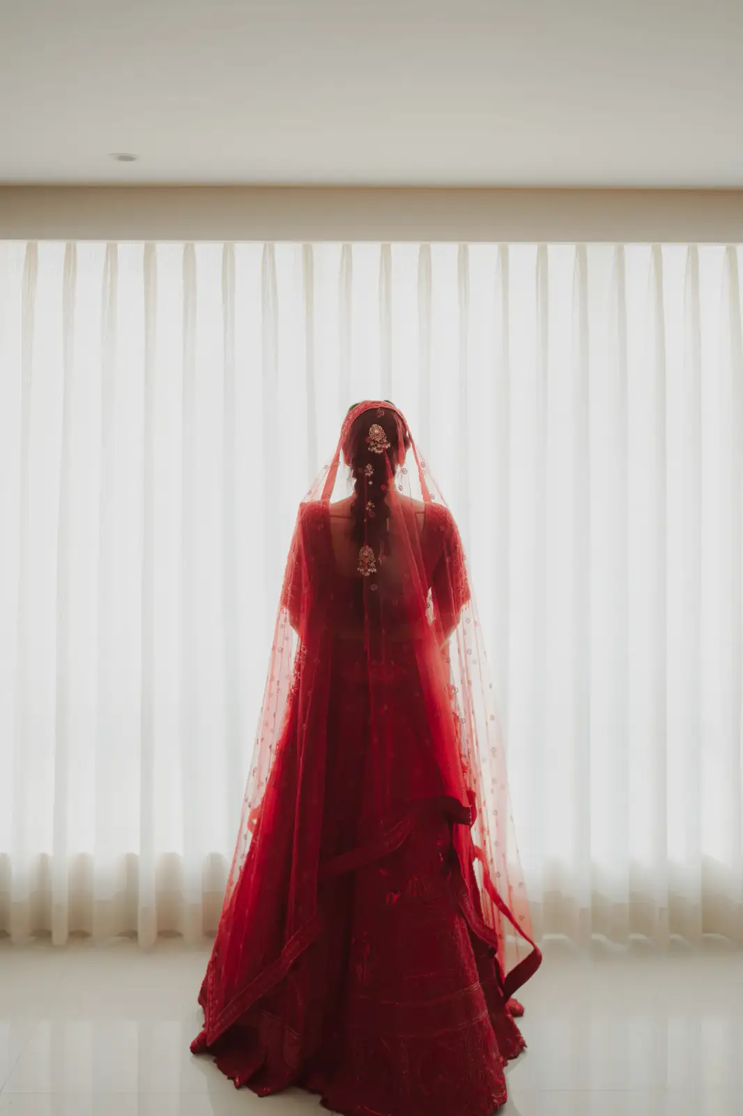 Bride in a red lehenga facing sheer curtains