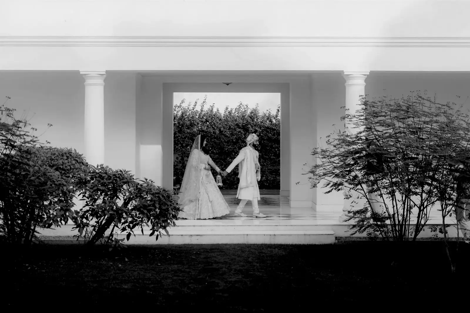 Couple walking hand in hand through a white colonnade
