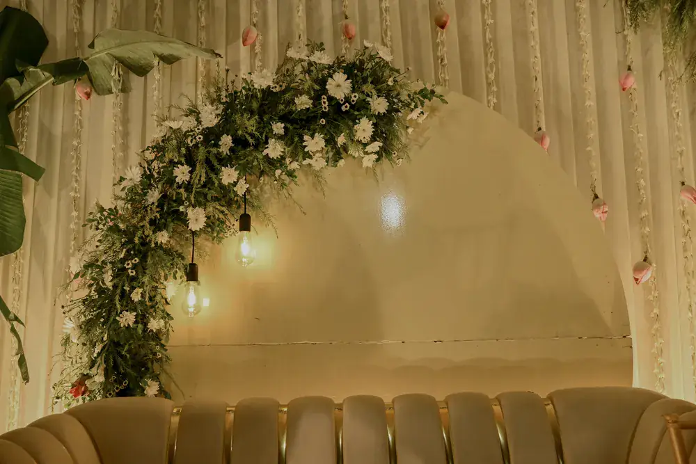 An ivory arch framed in white florals and warm bulbs above the stage sofa