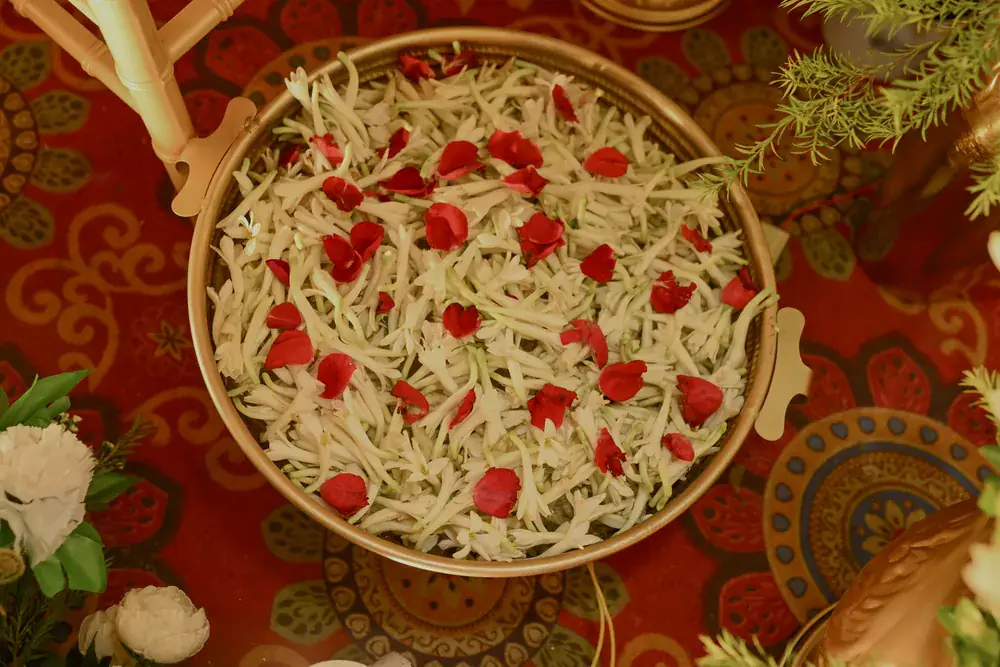 A brass platter of white flowers scattered with red rose petals