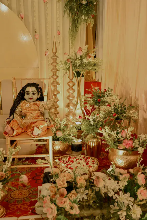 A traditional doll seated among brass urns and lilies