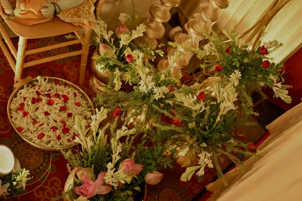 Lilies, greenery and a platter of rose petals beside brass urns