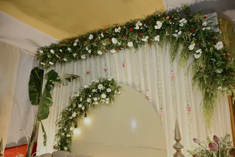 The stage canopy of white florals and greenery, lit warm