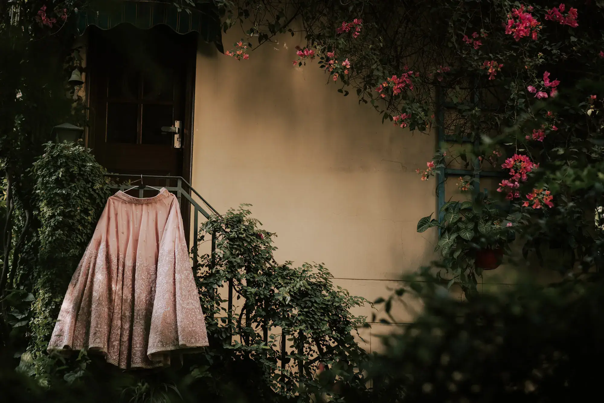 A bridal lehenga hung at a doorway framed by bougainvillea